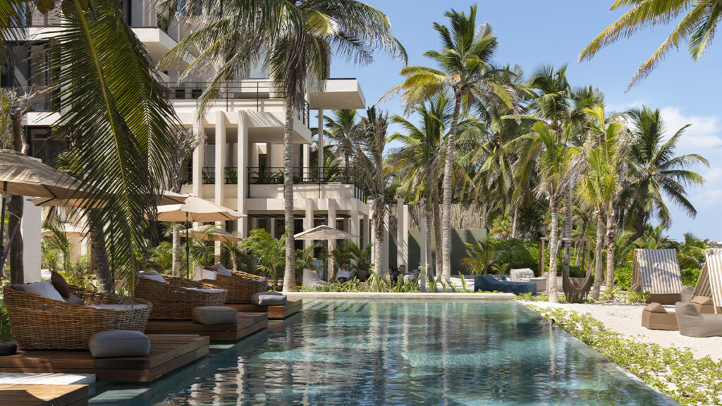 Vista exterior de Bespoke Tulum, con alberca y edificios de arquitectura contemporánea entre palmeras