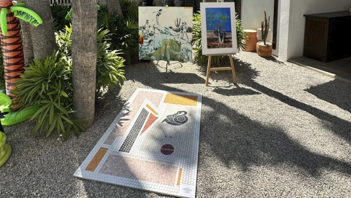 Instalación artística al aire libre con una obra colocada sobre el suelo y pinturas exhibidas en un jardín durante una edición de ABC ART BAJA CALIFORNIA.