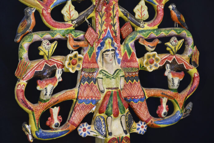 Figura de cerámica tipo árbol de la vida con una mujer al centro, rodeada de aves y animales coloridos sobre fondo oscuro.