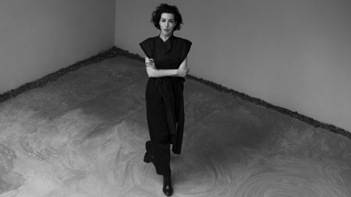 Jeannette Arévalo Angus de pie en una galería, vestida de negro, en un espacio minimalista de concreto