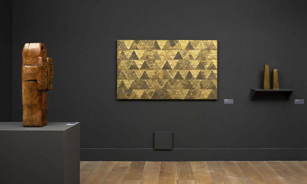 Vista a través de una puerta hacia una sala oscura con una obra de Francisco Toledo iluminada al fondo, junto a dibujos en una exposición de la colección Micha Levy en Madrid.