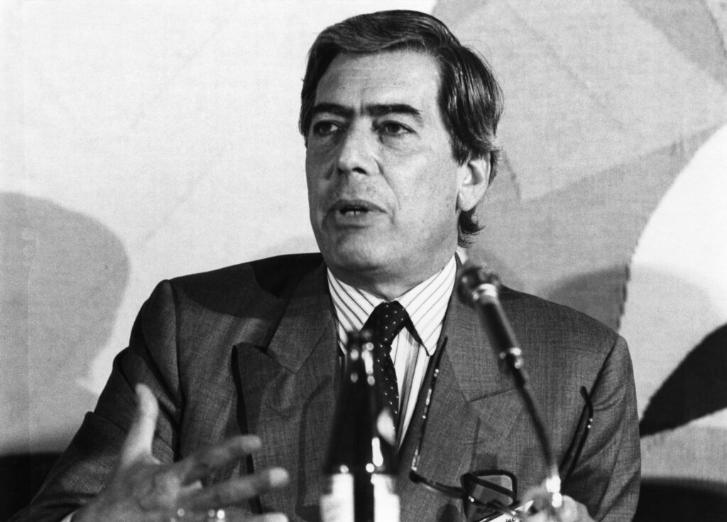 Retrato de Mario Vargas Llosa durante una intervención pública, con traje y corbata.