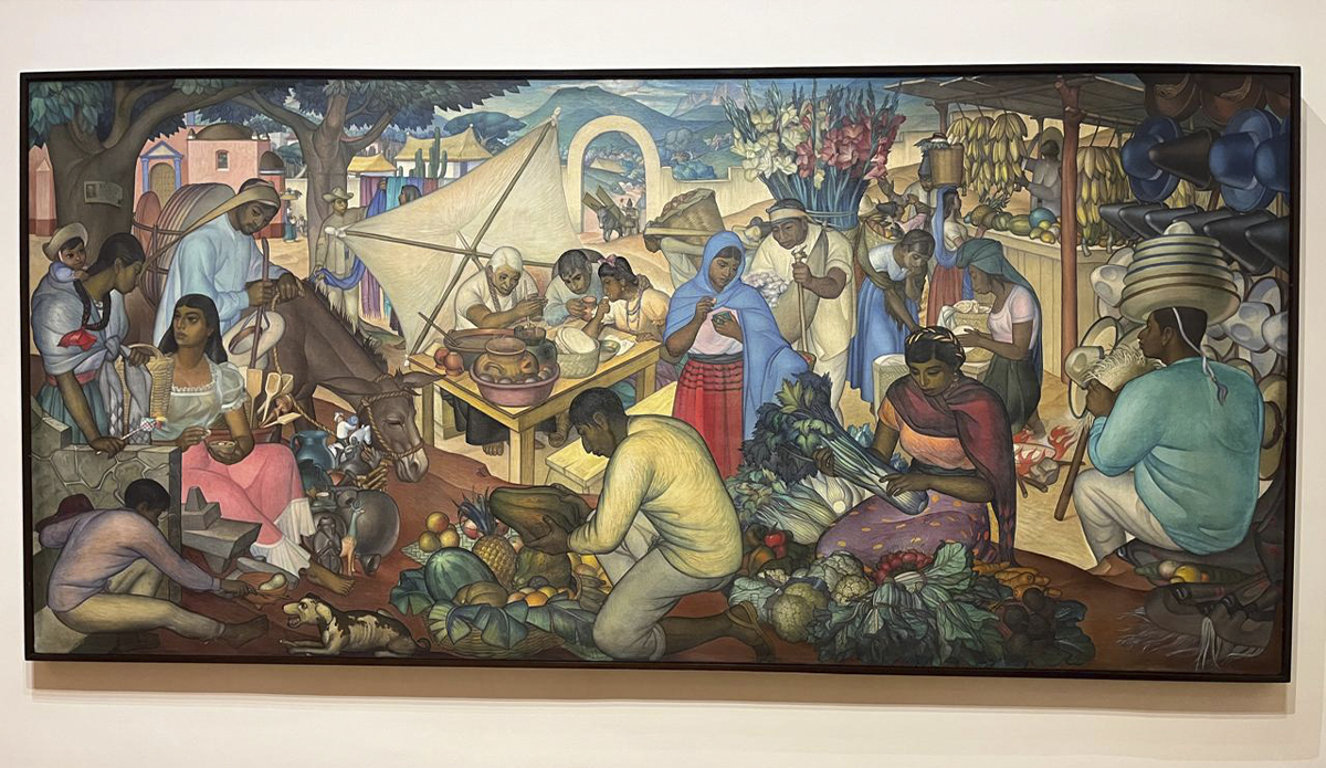 Mural colorido con vendedores, alimentos, flores y personajes en un mercado tradicional mexicano dentro de una sala de museo.