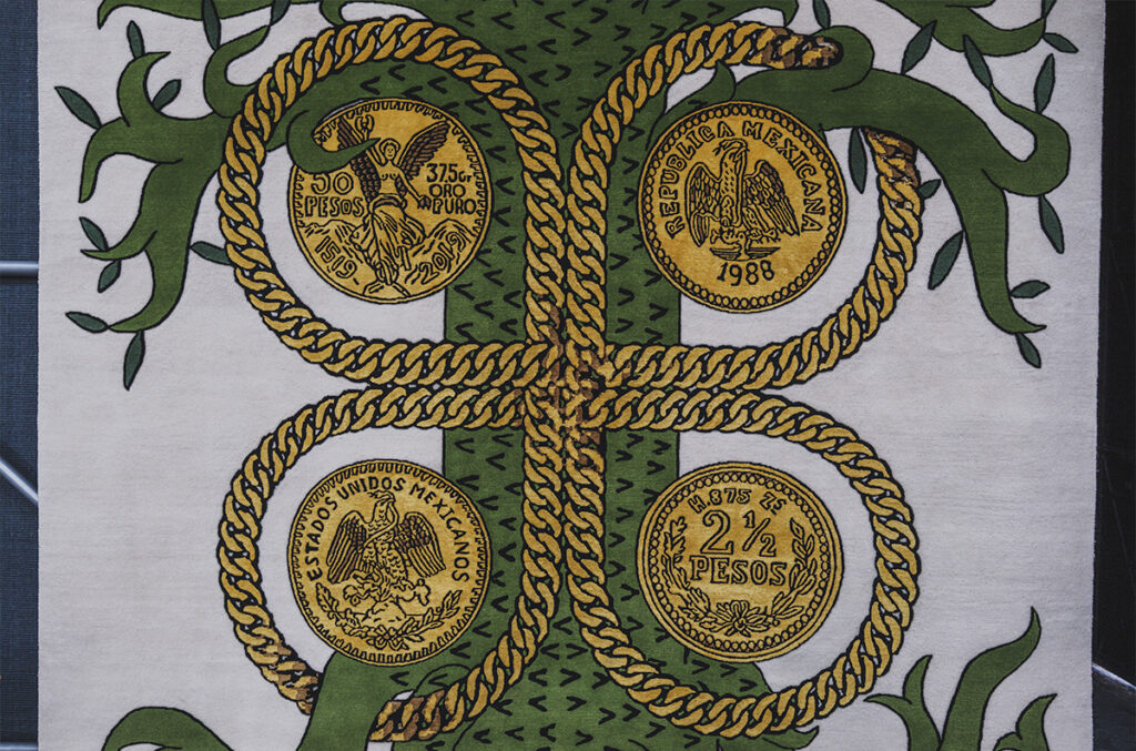 Tapete textil con una serpiente verde entrelazada con cadenas doradas y monedas mexicanas antiguas sobre fondo claro.