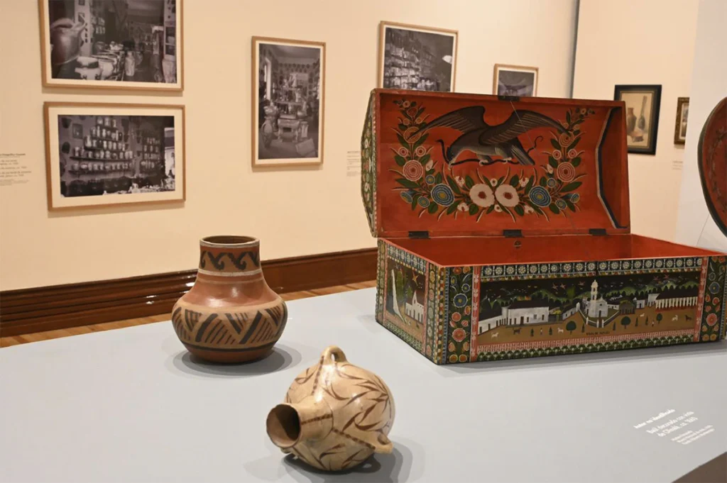 Caja artesanal pintada a mano y vasijas de barro sobre una vitrina dentro de un museo.