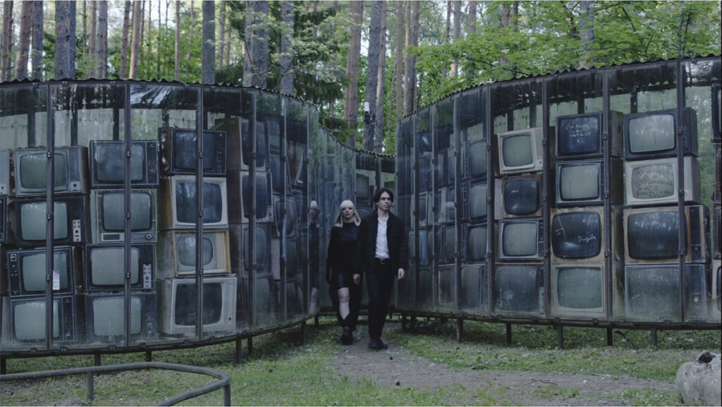Rogelio Serrano y Eglė Naujokaitytė caminando entre una instalación de televisores antiguos.