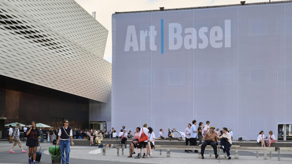 Entrada principal del recinto ferial de Art Basel 2026 en Basilea, con visitantes transitando frente a la fachada y el logo oficial del evento a gran escala.