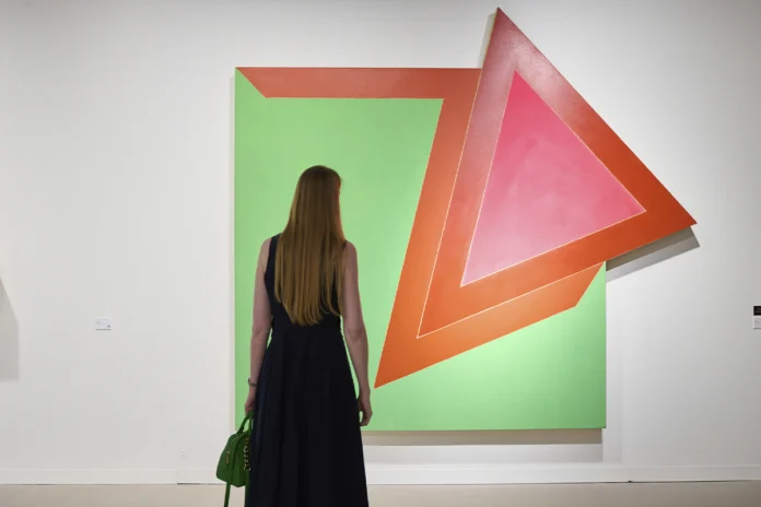 Una mujer de espaldas contempla una gran pintura abstracta y geométrica con tonos verdes, naranjas y rosas expuesta por la galería Elvira González en Art Basel 2026.