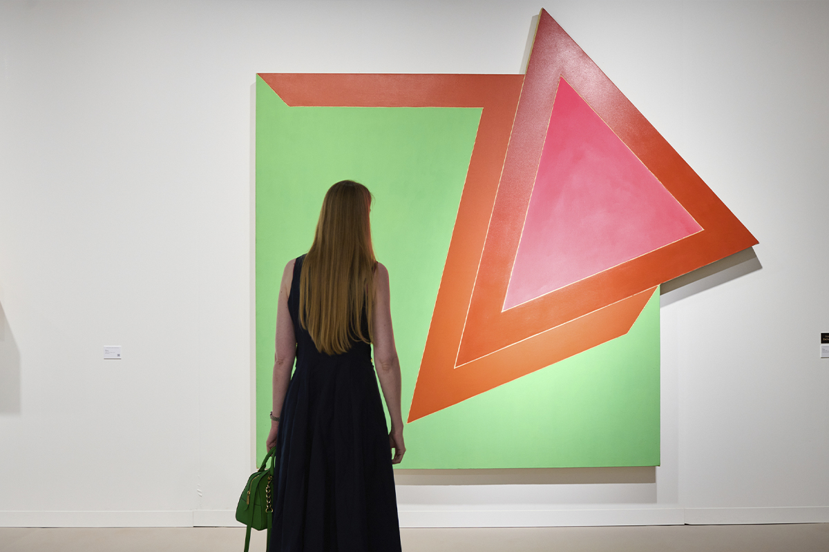 Una mujer de espaldas contempla una gran pintura abstracta y geométrica con tonos verdes, naranjas y rosas expuesta por la galería Elvira González en Art Basel 2026.