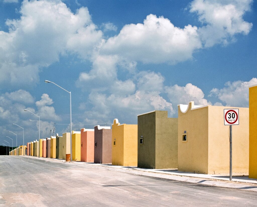 Fragmented Cities, Apodaca #2, de Alejandro Cartagena: calle con casas de colores bajo un cielo nublado.