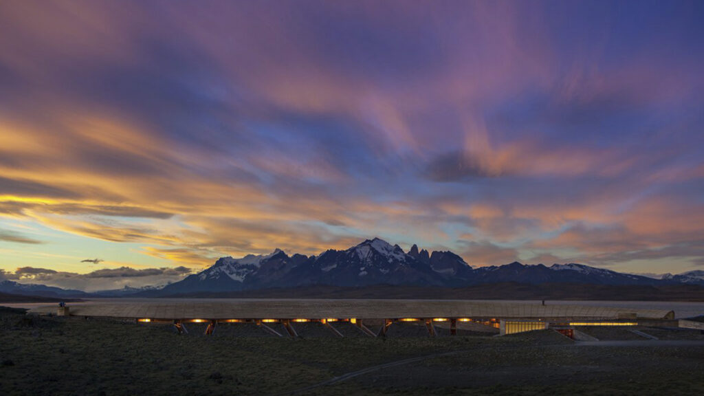 Vista aérea de Tierra Patagonia junto al lago Sarmiento, con las montañas de Torres del Paine al fondo durante el atardecer.