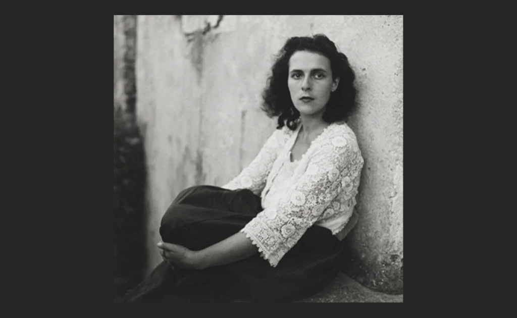 Leonora Carrington sentada junto a un muro en un retrato en blanco y negro durante su juventud.