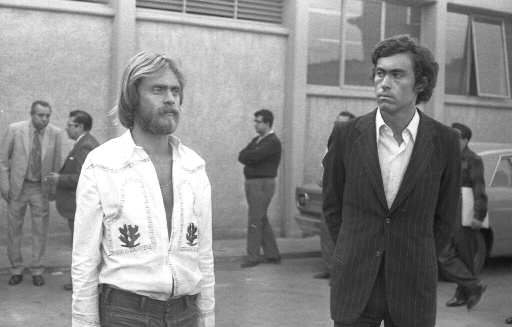 Fotografía de archivo en blanco y negro de 1971 que muestra a dos hombres en primer plano en un patio exterior.