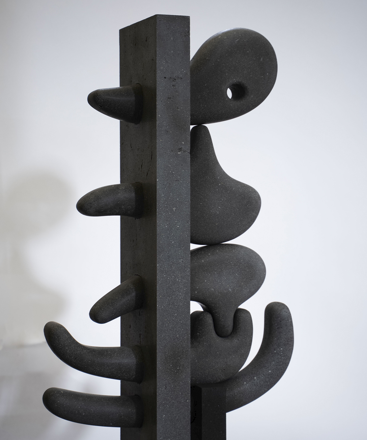 Detalle de una escultura de Pedro Reyes realizada en piedra volcánica oscura. La obra presenta formas orgánicas y biomórficas que se ensamblan alrededor de una estructura vertical geométrica, explorando la relación entre la talla directa, la permanencia material y las tradiciones escultóricas mesoamericanas.