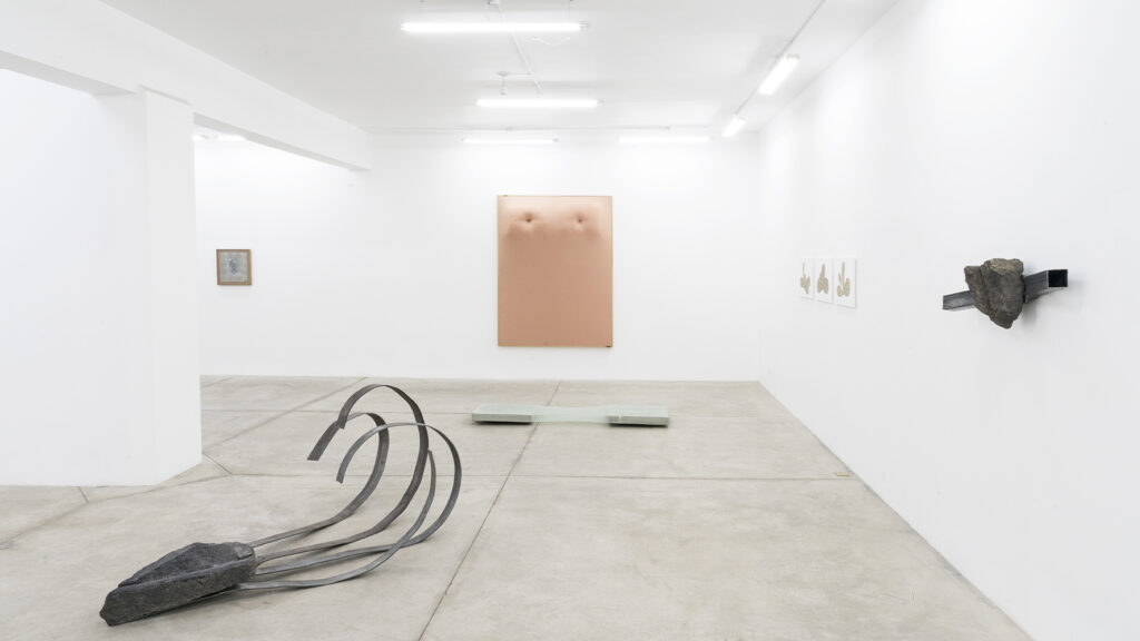 Vista amplia de una galería de arte contemporáneo con esculturas e instalaciones distribuidas en una sala minimalista de paredes blancas y piso de concreto pulido.