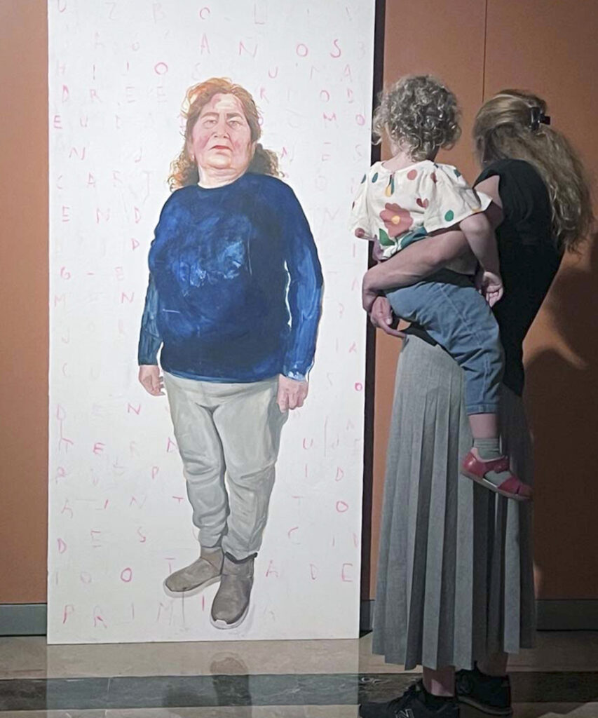 Una visitante sostiene a un niño mientras observa el retrato de una trabajadora doméstica latinoamericana en la exposición Cama Adentro.