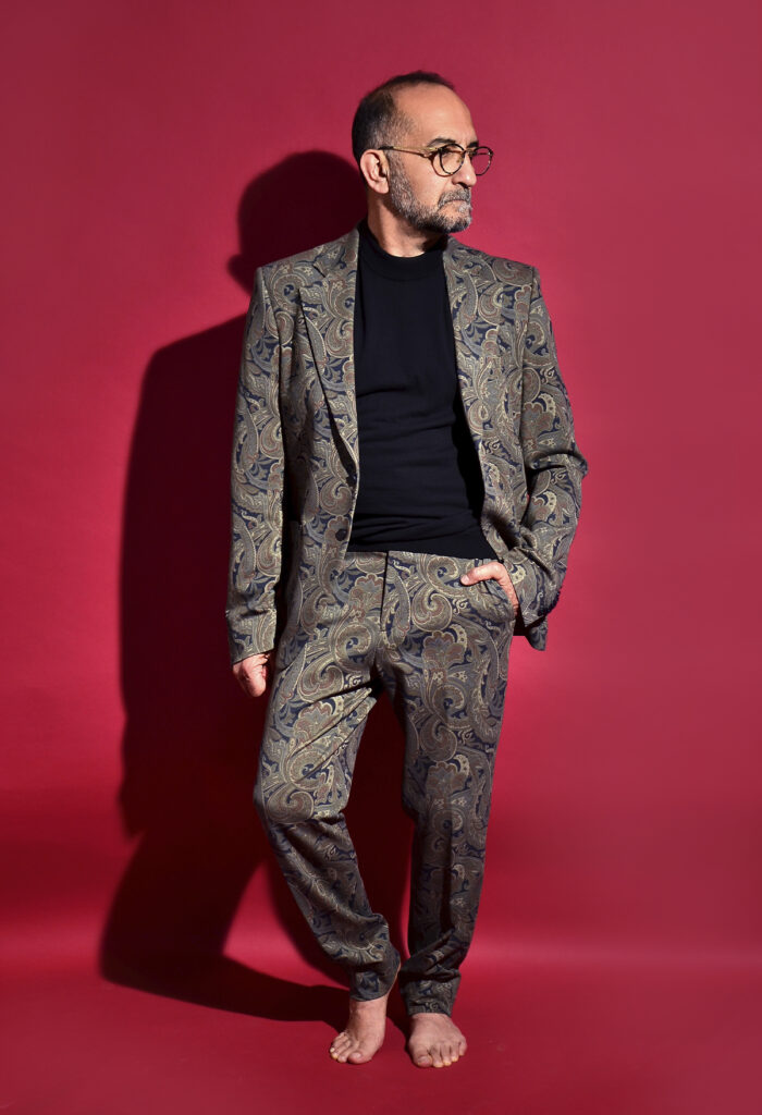 Retrato de Gabriel Sánchez Viveros con traje de estampado paisley sobre fondo rojo.