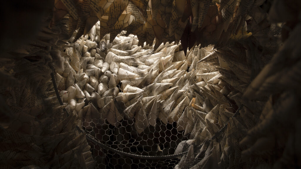Instalación inmersiva de Nebraska Flores Espín compuesta por cientos de piezas de papel enrollado suspendidas sobre una estructura de malla metálica, inspirada en formas orgánicas y hábitats naturales.