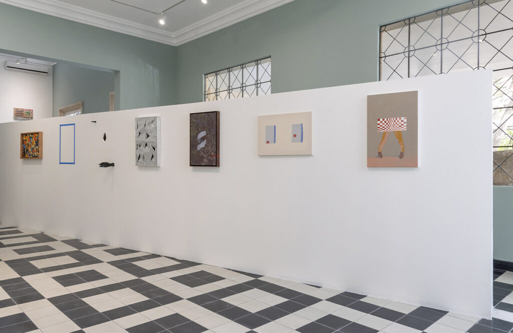 Obras de arte contemporáneo de distintos formatos exhibidas sobre un muro blanco en una sala de exposición.