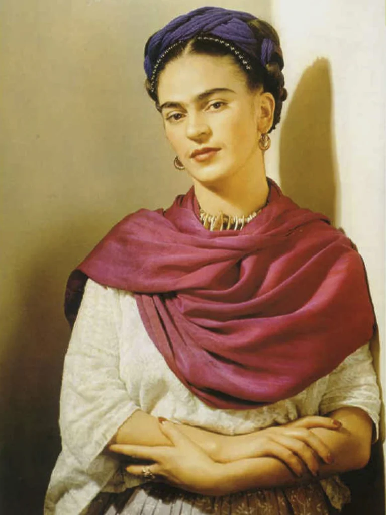 Retrato de Frida Kahlo vistiendo un rebozo color magenta y un tocado azul. La artista aparece con una expresión serena y la vestimenta que contribuyó a convertirla en uno de los mayores íconos culturales de México.