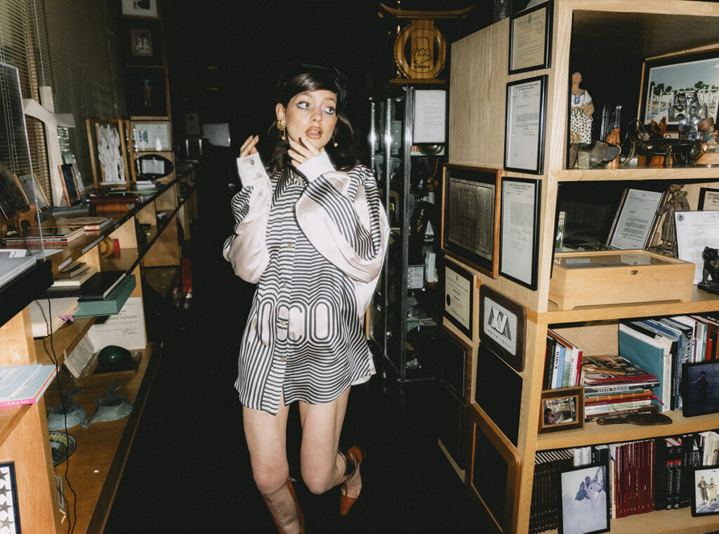 Modelo porta una camisa con gráficos inspirados en México 68, diseñada por Gabrielle Venguer y fotografiada en el estudio de Pedro Ramírez Vázquez, rodeada de libros, documentos y objetos que forman parte de su archivo personal.