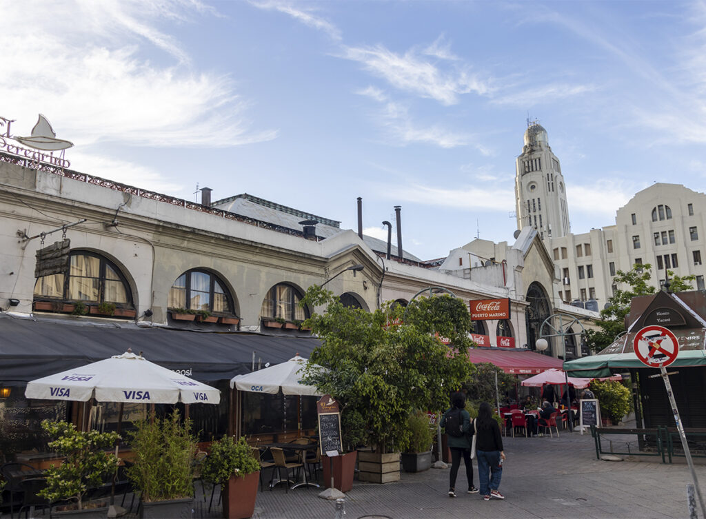 Mercado del Puerto de Montevideo con terrazas, restaurantes y el Palacio Salvo al fondo.