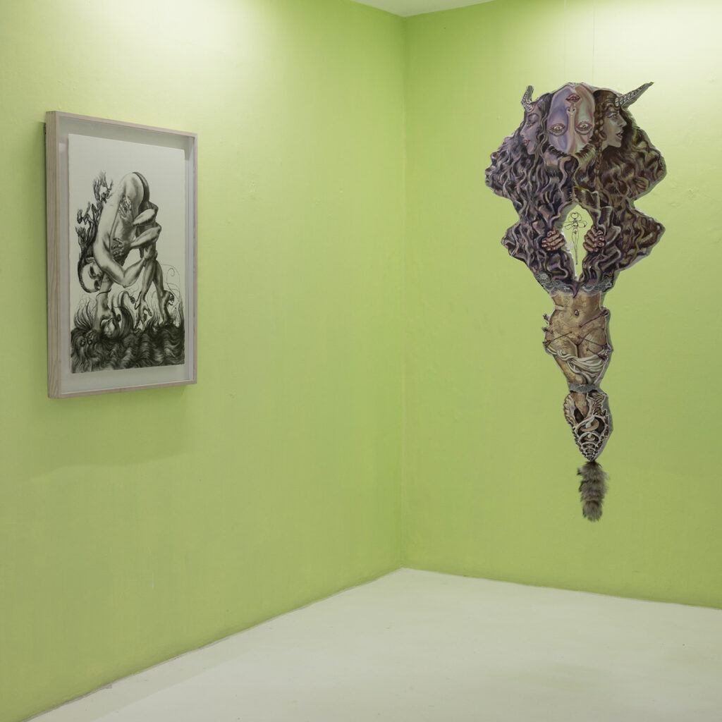 Sala de exposición con un dibujo enmarcado y una escultura suspendida sobre un muro verde.