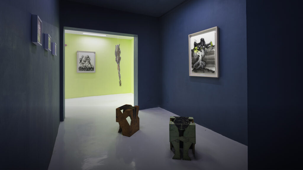 Obras de arte contemporáneo de diferentes técnicas exhibidas sobre un muro blanco en una exposición colectiva.