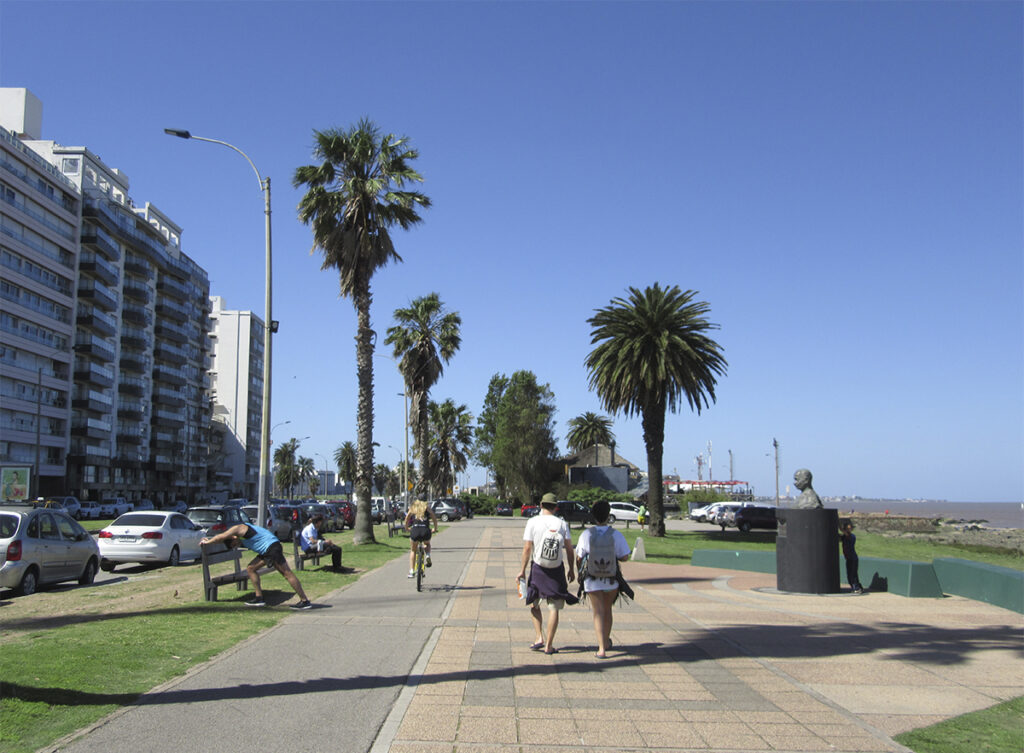 Personas caminan y andan en bicicleta sobre la Rambla de Montevideo frente al Río de la Plata.