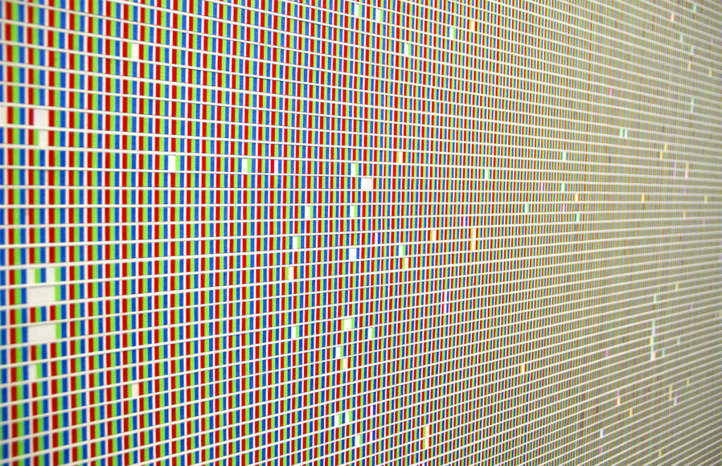 A close-up view of a work consisting of a grid of lines and small red, green, and blue segments that evoke the structure of a digital screen.
