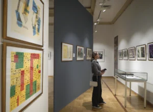 Visitante observa una selección de obras de arte moderno, entre pinturas y obra gráfica, expuestas en la pared de una sala de museo.