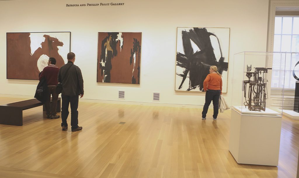 Visitantes observan pinturas y esculturas expuestas en una sala de museo dedicada al arte moderno.