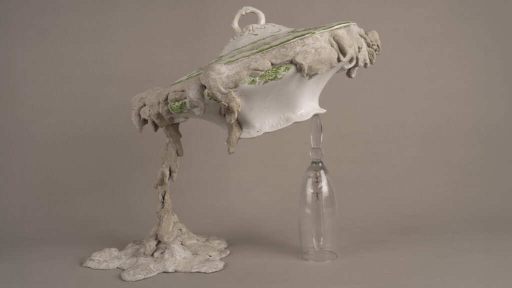 Sopera de porcelana blanca y verde intervenida con cemento y sostenida por una pieza de vidrio.