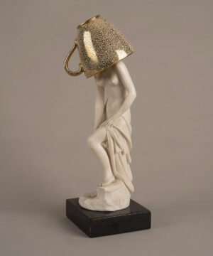 Figura escultórica femenina sobre una base oscura, intervenida con una taza de acabado dorado que cubre la cabeza. La pieza forma parte de Escenarios domésticos, proyecto en el que Marianna Dellekamp transforma objetos provenientes de su archivo familiar para explorar la memoria y los vínculos afectivos con las pertenencias.
