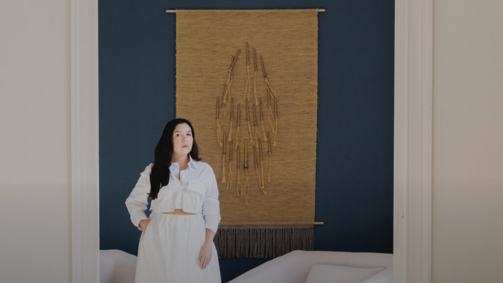 Retrato de Juliana Sorondo de pie frente a una obra textil en el interior de la galería.