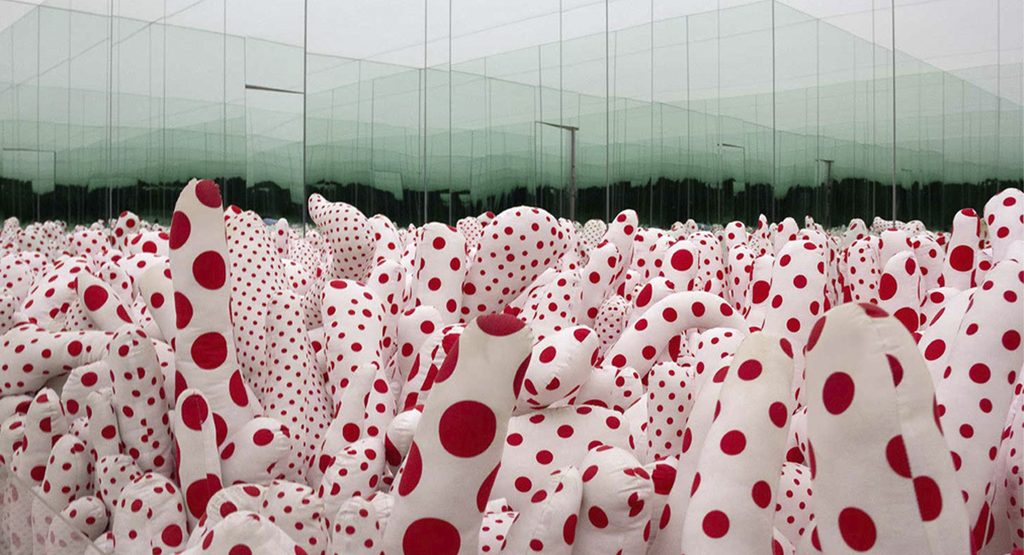 Instalación de Yayoi Kusama con numerosas formas blandas blancas cubiertas de lunares rojos y multiplicadas por paredes de espejo.