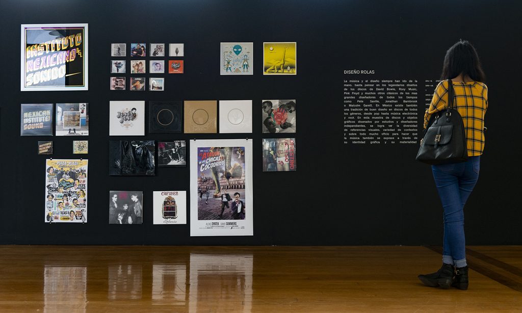 Visitante observa carteles y piezas de diseño gráfico expuestos sobre un muro negro.