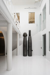 Espacio blanco de Alzueta Gallery con dos esculturas oscuras y una escalera.
