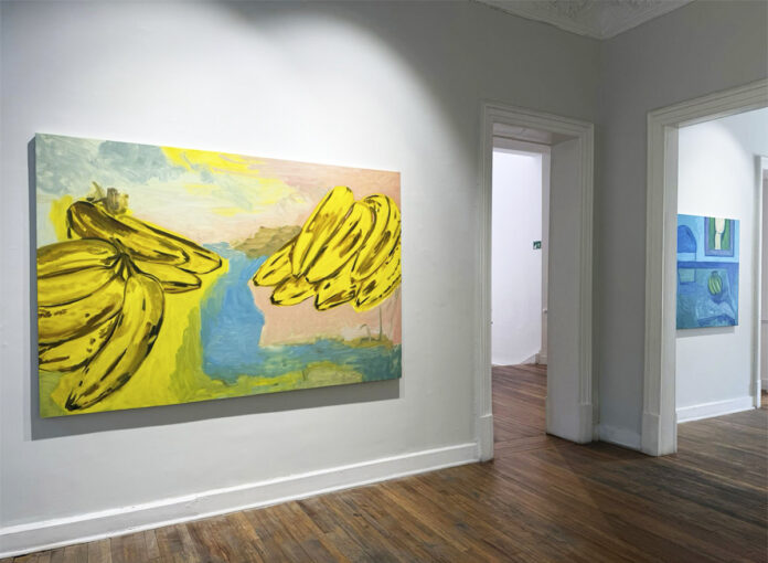 Pintura de Emi Winter con grandes racimos de plátanos amarillos, presentada en la exposición Trópico de Jersey en Galería Ethra.