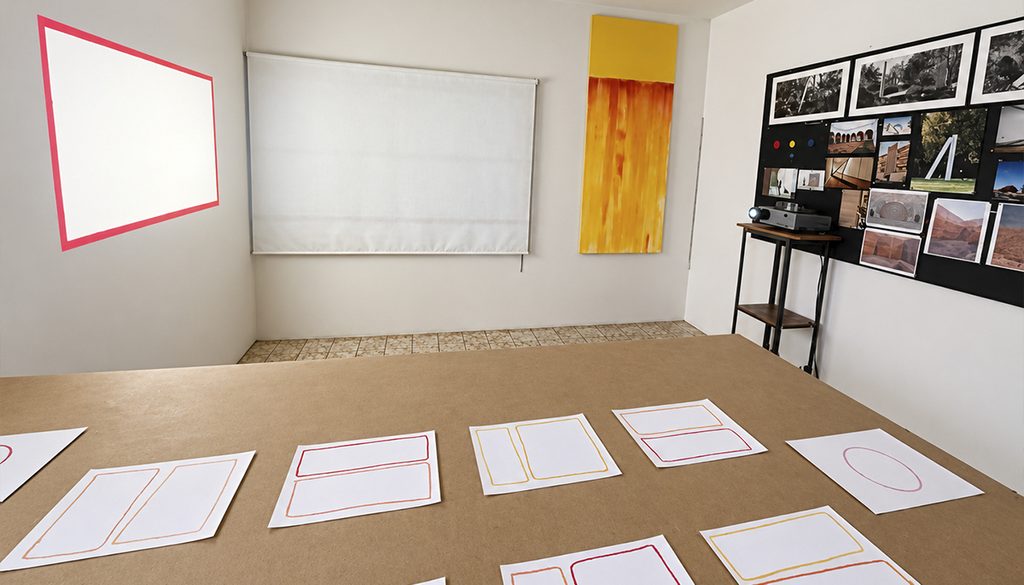 Una toma amplia del interior del estudio de arte de Francisco Ugarte. En el centro, una gran mesa de trabajo de madera rústica está llena de materiales de arte, herramientas, maquetas de arquitectura y bocetos.