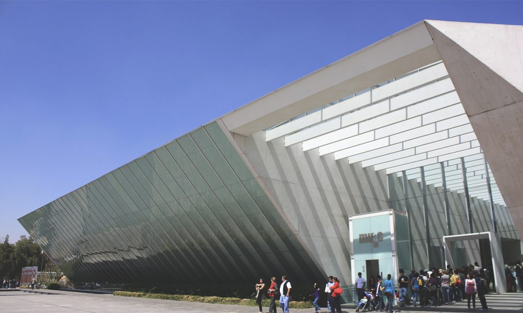 The MUAC's glass-and-concrete facade under a blue sky, with visitors gathered in front of the museum's entrance.