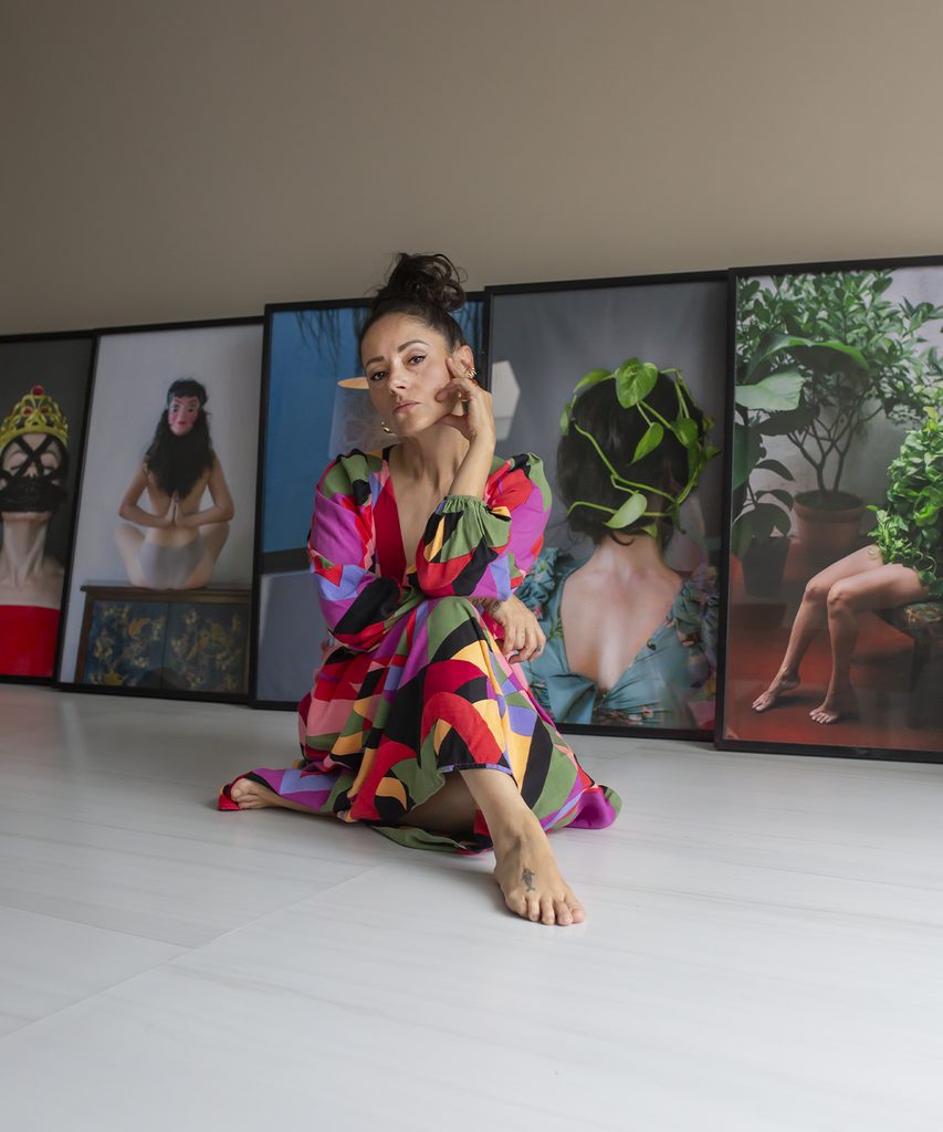 Azz Rodríguez sentada en el suelo frente a varias fotografías de gran formato pertenecientes a su obra de autorretrato.