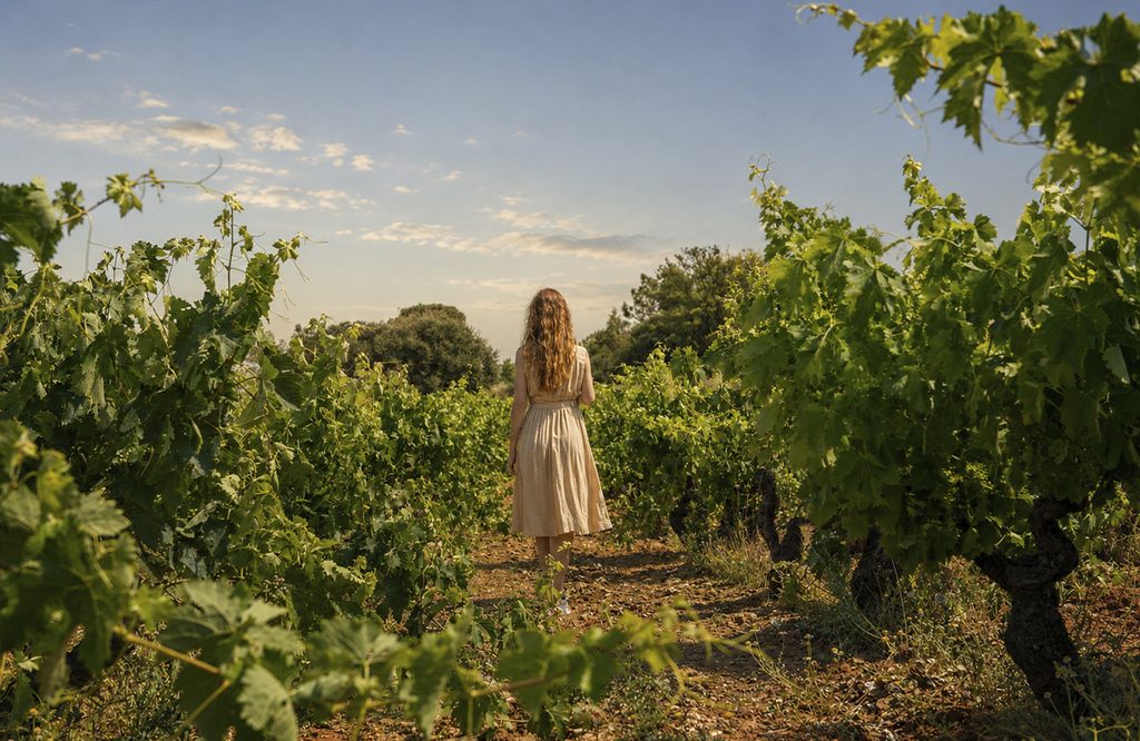 A woman standing among rows of green vineyards during a wine-tasting tour in the Ribera del Duero.
