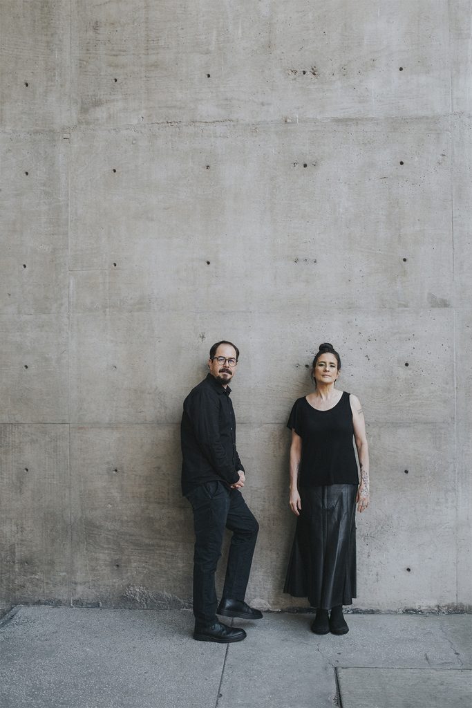 Jorge Camacho y Karla Paniagua posan frente a un muro de concreto.