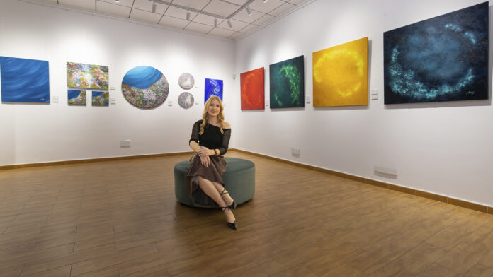 Mariam Cremades sitting in her gallery in Alicante, surrounded by abstract paintings.