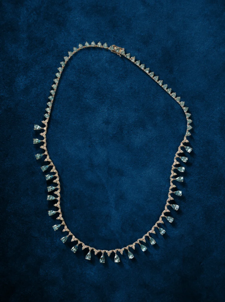 Collar de oro blanco con aguamarinas azules y diamantes sobre un fondo azul oscuro.