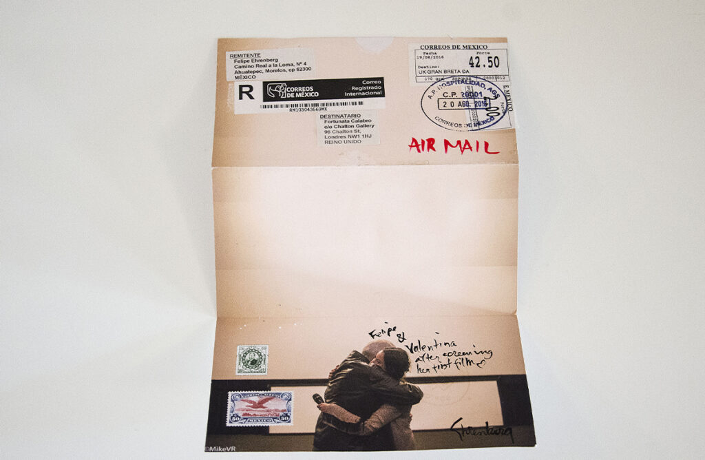 Pieza postal con etiquetas de Correos de México, anotaciones manuscritas y una fotografía de dos personas abrazándose.