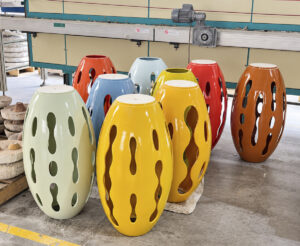 Piezas ovaladas de cerámica en verde claro, amarillo, azul, rojo y naranja, con perforaciones alargadas, sobre el piso del taller.
