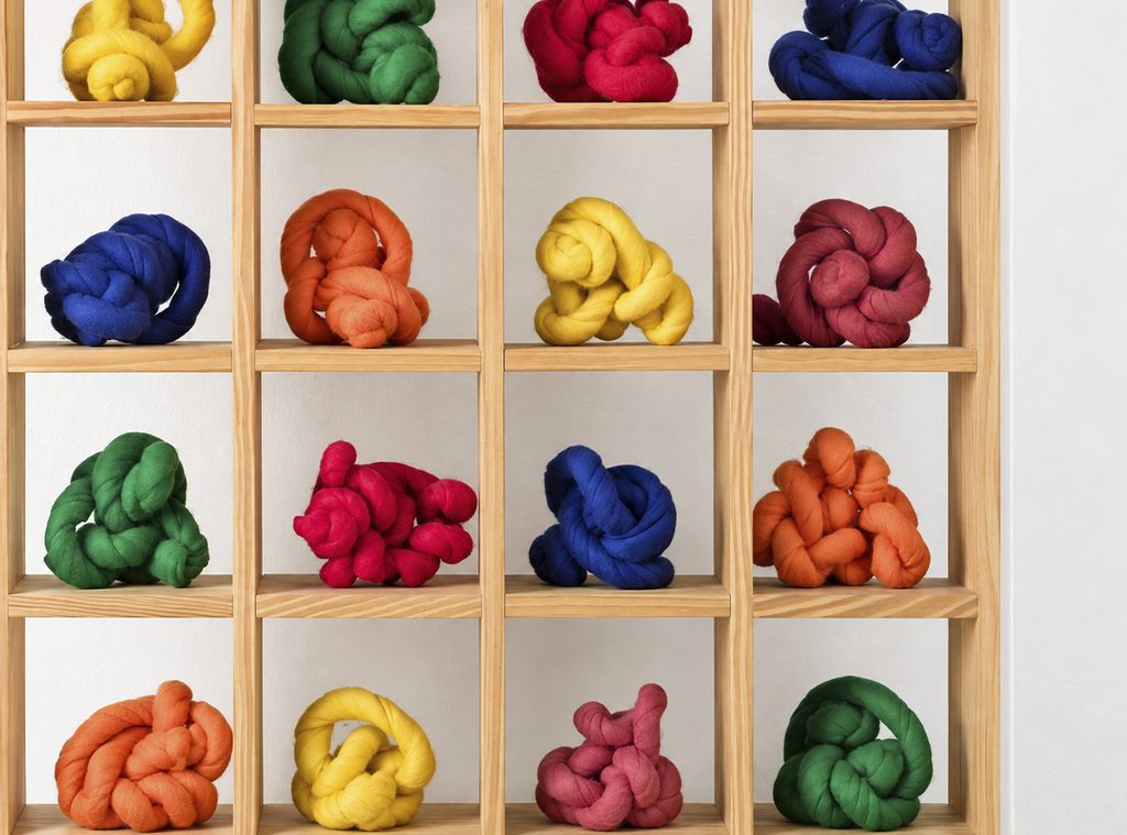 A composition of sixteen wooden compartments with knotted shapes in yellow, green, red, blue, and orange.