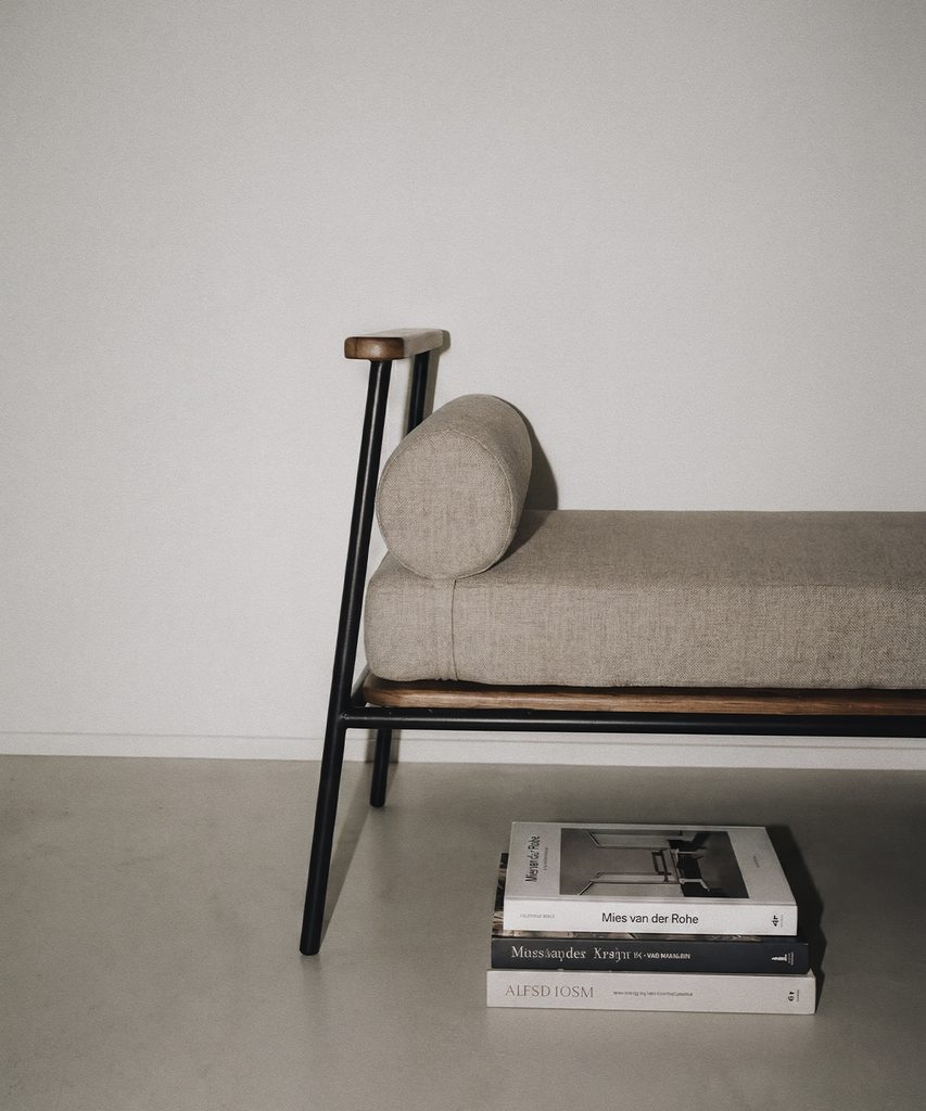 Silla de Dórica con tapizado beige, respaldo curvo y patas de madera oscura junto a una pila de libros de diseño.